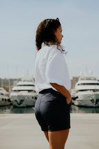Woman standing on a dock with boats in the background wearing a pair of women's navy chino deck shorts.