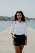 Woman standing on a pier by a body of water wearing a pair of women's navy chino deck shorts.