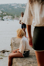 Two people by a waterfront with a scenic background. Woman wearing board shorts / running shorts. Yachtwear. Women's deck shorts.