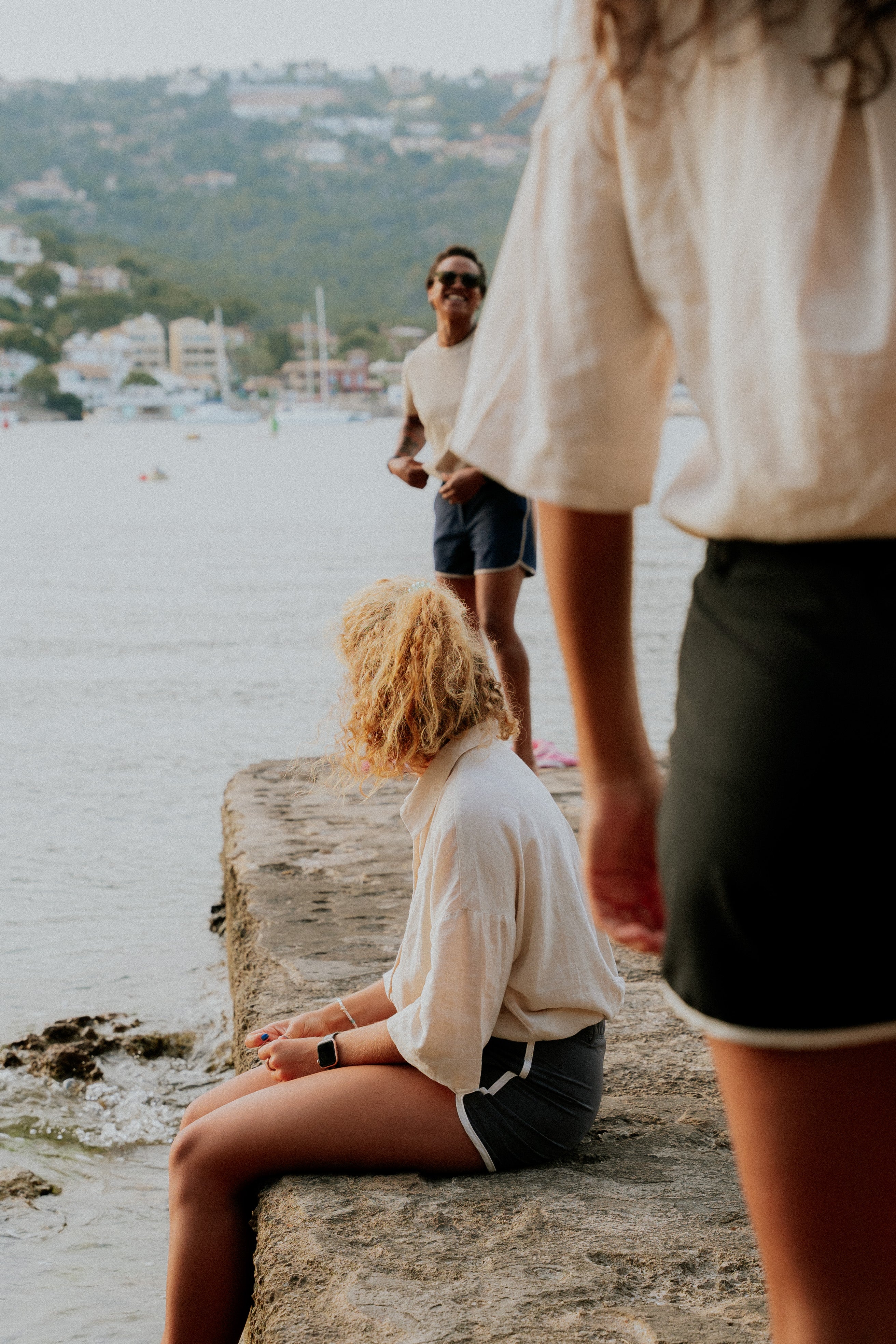 Two people by a waterfront with a scenic background. Woman wearing board shorts / running shorts. Yachtwear. Women's deck shorts.