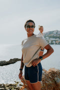 Two women standing on a cliff overlooking the water wearing a pair of navy women's board shorts with white piping.