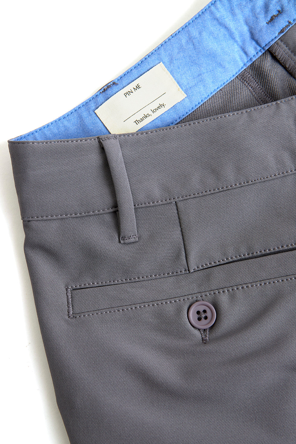 Close-up of gray pants with a button and label on a white background.
Yachtwear. Workwear. Grey Chino Shorts