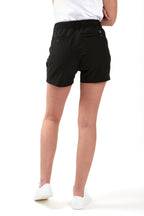 Woman wearing a white polo shirt and black chino shorts on a white background. Women's deck shorts. Yachtwear, workwear