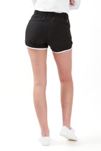 Woman wearing a white long-sleeve top and black shorts on a white background. Women's deck shorts. Yachtwear, workwear