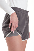 Woman wearing a white long-sleeve top and gray shorts on a white background. Women's deck shorts. Yachtwear, workwear