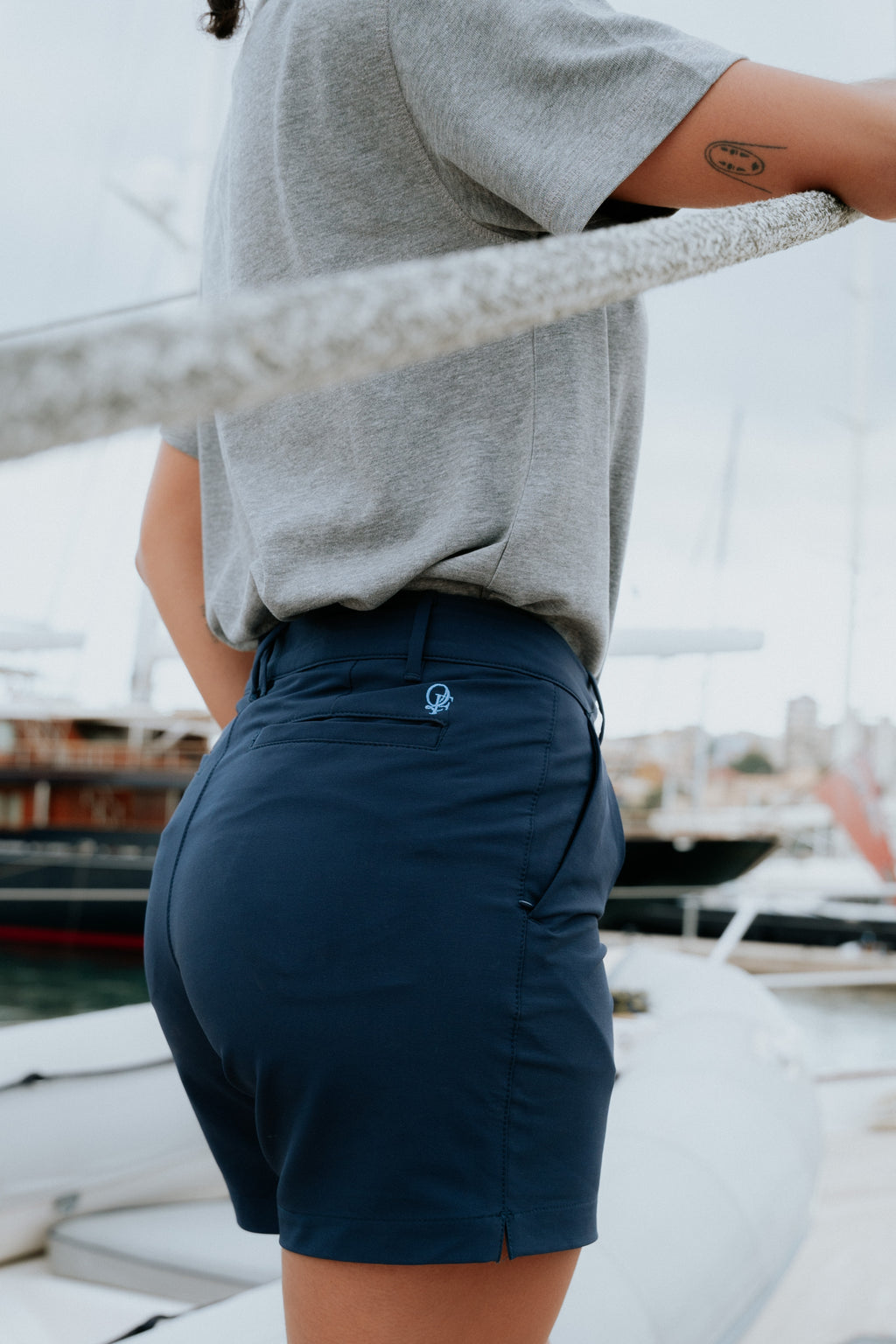 Person wearing navy chino shorts and a gray shirt with a marina background. Yachtwear. Women's deck Shorts.