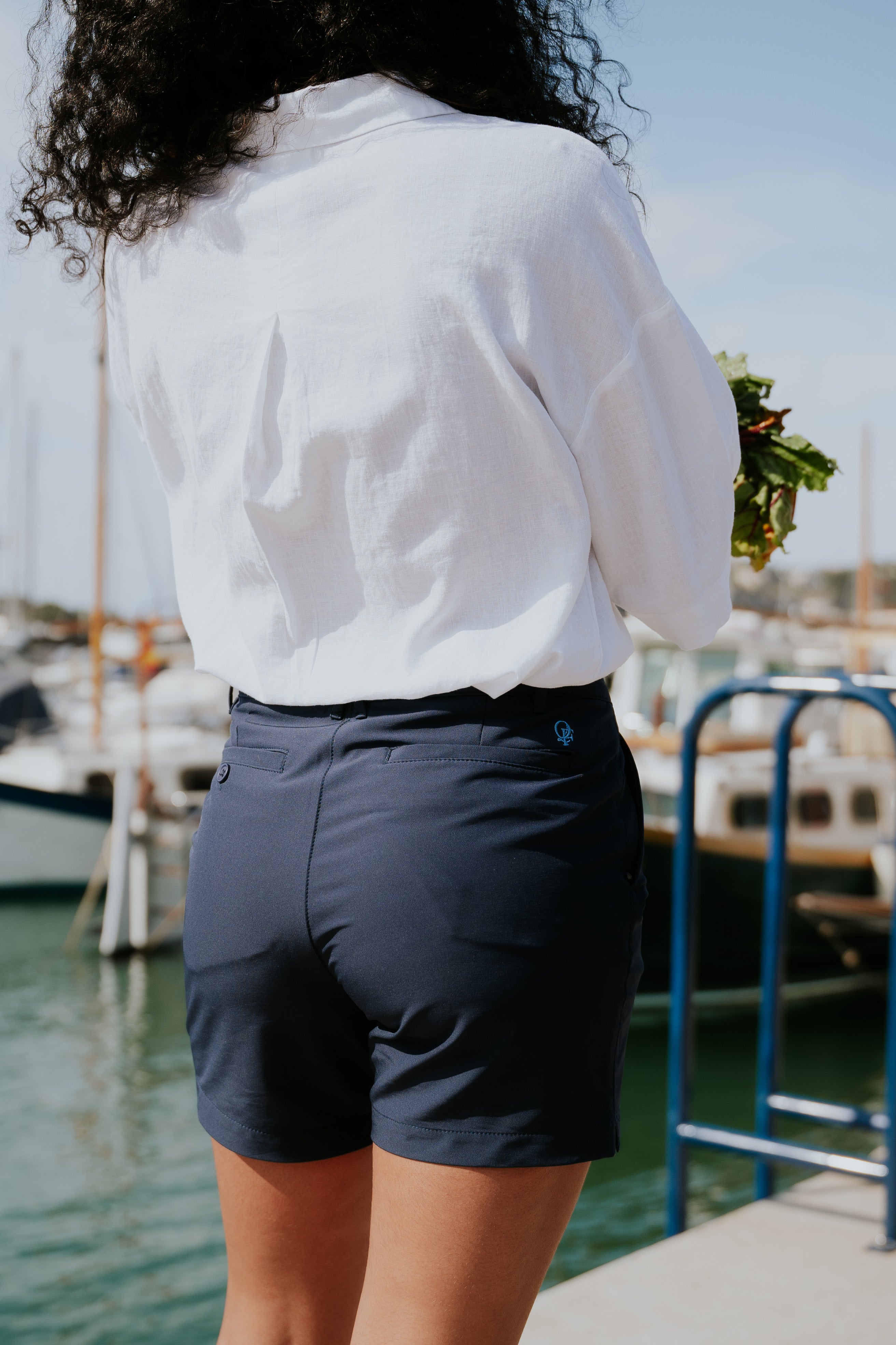 Person wearing a white shirt and navy chino shorts in a marina. Yachtwear. Women's Deck Shorts.